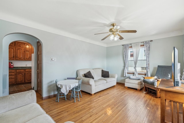 living area with ceiling fan, baseboards, arched walkways, and light wood-style flooring