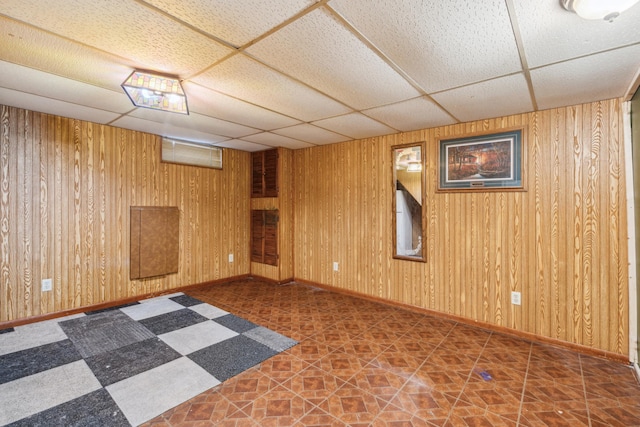 unfurnished room with tile patterned floors, wood walls, a paneled ceiling, and baseboards