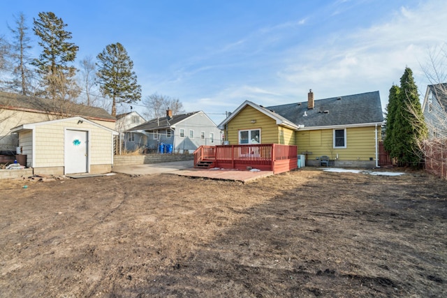 back of house featuring an outbuilding, a deck, a storage shed, a shingled roof, and a chimney