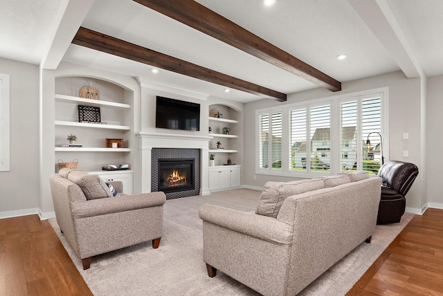 living room with built in shelves, light hardwood / wood-style flooring, and beamed ceiling