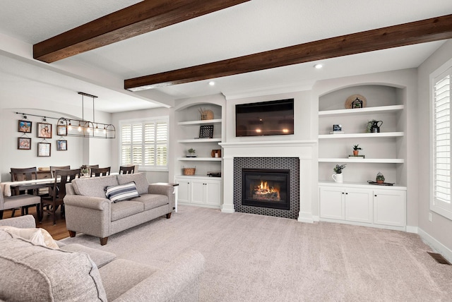 living room featuring a tiled fireplace, light carpet, built in features, and beamed ceiling