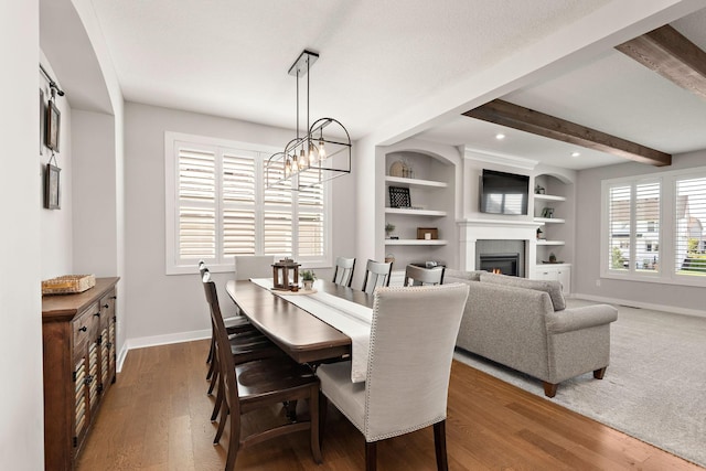 dining space with dark hardwood / wood-style flooring, an inviting chandelier, beam ceiling, and built in shelves