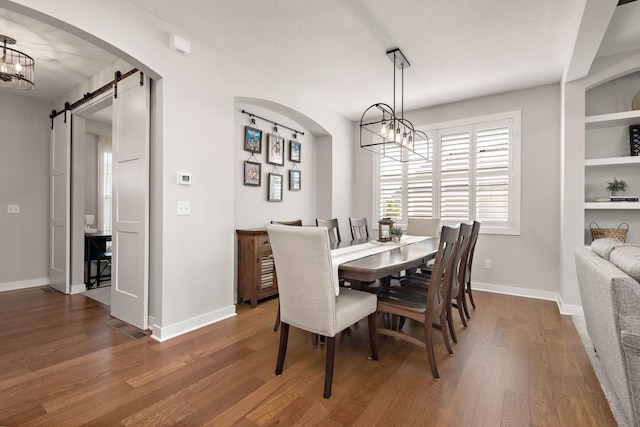 dining room featuring dark wood-type flooring, a barn door, and a chandelier