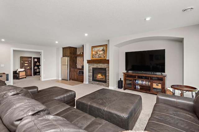 living room with a stone fireplace, light colored carpet, and a textured ceiling