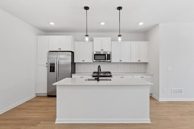 kitchen featuring stainless steel appliances, visible vents, an island with sink, and light wood-style flooring