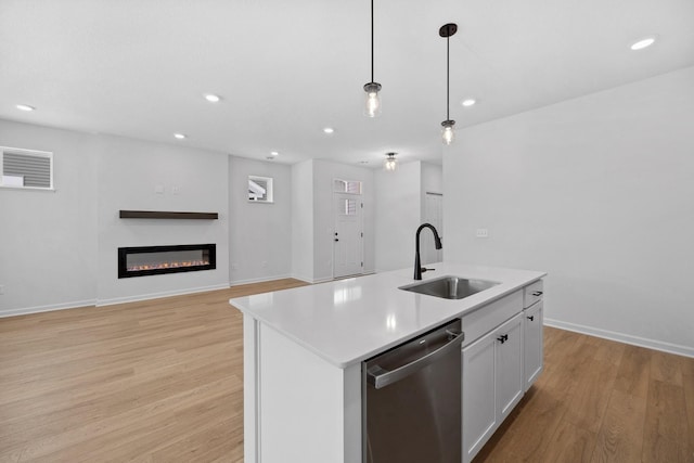 kitchen with a glass covered fireplace, a sink, pendant lighting, dishwasher, and light wood-type flooring