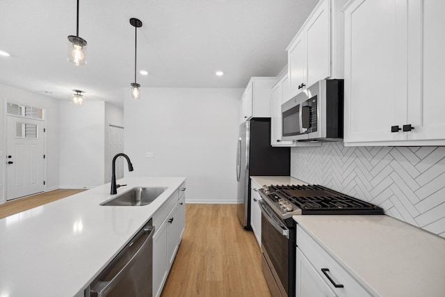 kitchen with a sink, decorative backsplash, light countertops, appliances with stainless steel finishes, and pendant lighting