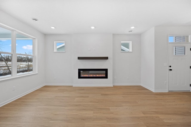 unfurnished living room with a glass covered fireplace, recessed lighting, light wood-type flooring, and baseboards