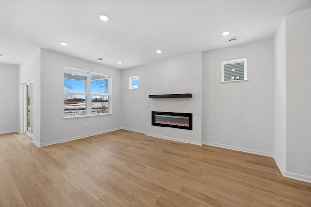 unfurnished living room featuring a glass covered fireplace, recessed lighting, baseboards, and light wood finished floors