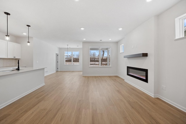 unfurnished living room featuring baseboards, light wood-style flooring, recessed lighting, a glass covered fireplace, and a chandelier