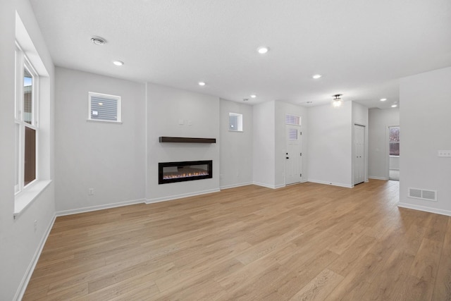 unfurnished living room with light wood-type flooring, visible vents, a glass covered fireplace, and recessed lighting