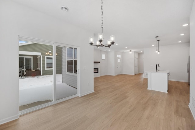 interior space featuring baseboards, recessed lighting, light wood-style floors, a glass covered fireplace, and a sink