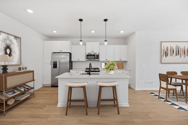 kitchen with tasteful backsplash, an island with sink, light wood-style floors, stainless steel appliances, and a sink