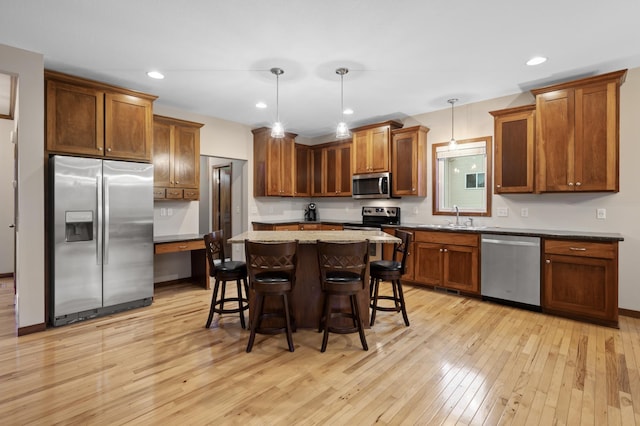 kitchen with appliances with stainless steel finishes, a kitchen breakfast bar, a center island, light wood-style floors, and a sink