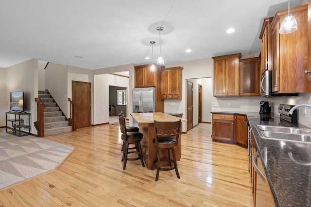 kitchen with a center island, light wood-style flooring, appliances with stainless steel finishes, brown cabinetry, and a sink