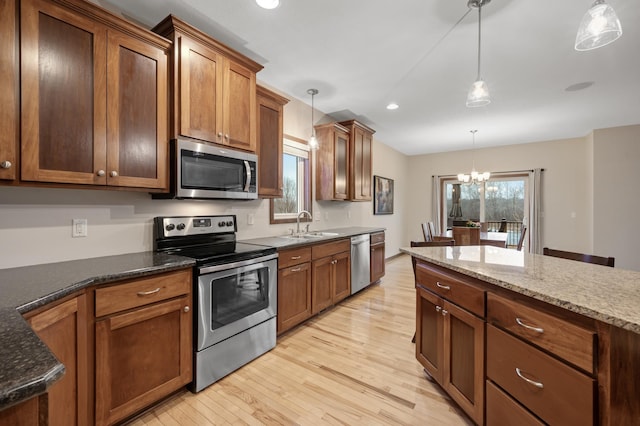 kitchen featuring light wood-style flooring, appliances with stainless steel finishes, dark stone countertops, hanging light fixtures, and a sink