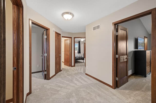 corridor featuring baseboards, a textured ceiling, visible vents, and light colored carpet