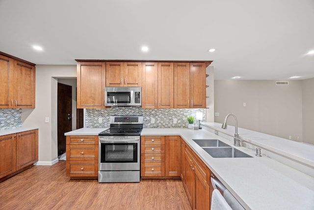 kitchen featuring stainless steel appliances, brown cabinetry, light wood-type flooring, and a sink