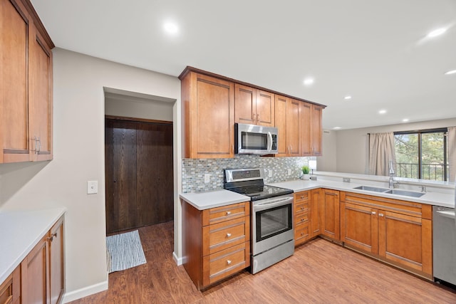 kitchen with a sink, light countertops, appliances with stainless steel finishes, tasteful backsplash, and light wood-type flooring