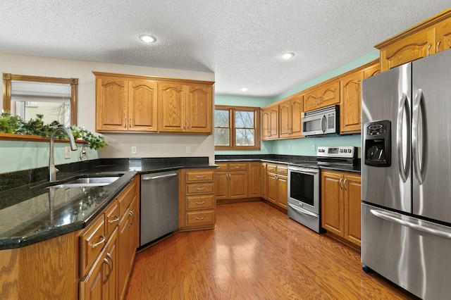 kitchen featuring sink, a textured ceiling, dark stone countertops, stainless steel appliances, and light hardwood / wood-style floors