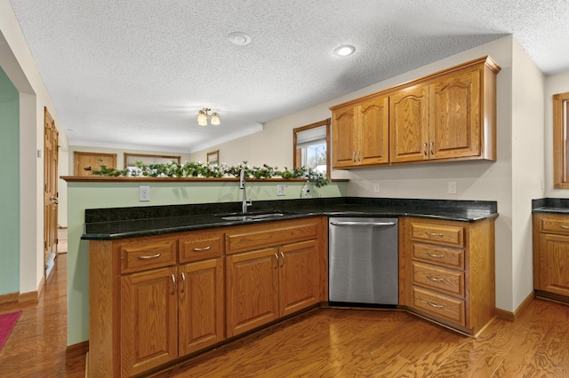 kitchen with sink, dark stone counters, stainless steel dishwasher, light hardwood / wood-style floors, and kitchen peninsula