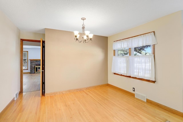 empty room with hardwood / wood-style flooring, a textured ceiling, a fireplace, and an inviting chandelier