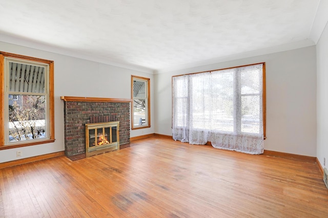 unfurnished living room featuring hardwood / wood-style flooring, a brick fireplace, crown molding, and baseboards