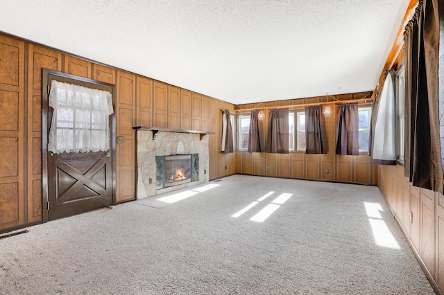 unfurnished living room featuring a glass covered fireplace, light colored carpet, wood walls, and a textured ceiling