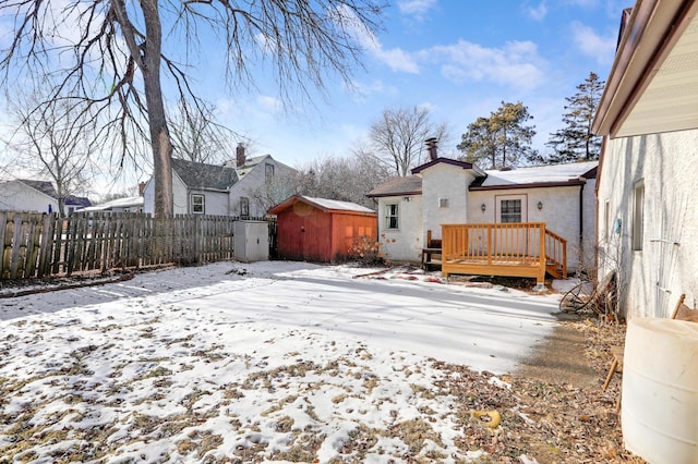 yard covered in snow featuring an outbuilding, fence, a shed, and a wooden deck