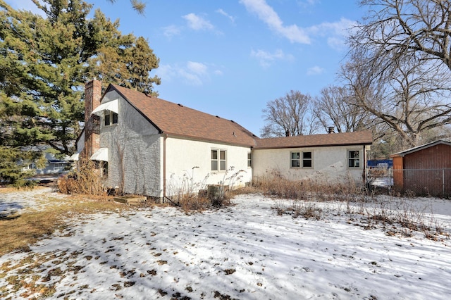 snow covered property with stucco siding and a chimney