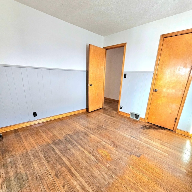 unfurnished bedroom with visible vents, a textured ceiling, a wainscoted wall, and hardwood / wood-style flooring