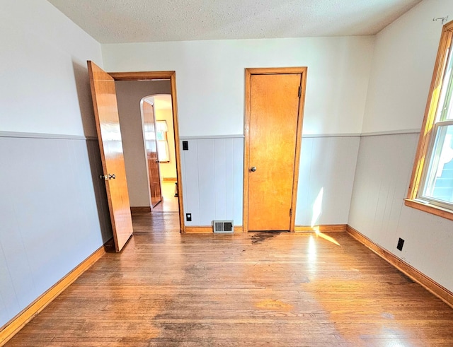 unfurnished bedroom with visible vents, arched walkways, a textured ceiling, and wood finished floors