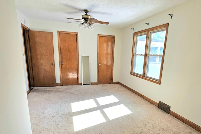 unfurnished bedroom with a textured ceiling, baseboards, visible vents, light carpet, and two closets