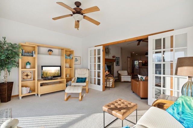 living room featuring a ceiling fan, french doors, light colored carpet, and a lit fireplace