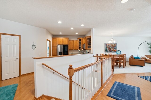 kitchen featuring light wood finished floors, glass insert cabinets, an inviting chandelier, stainless steel refrigerator with ice dispenser, and recessed lighting