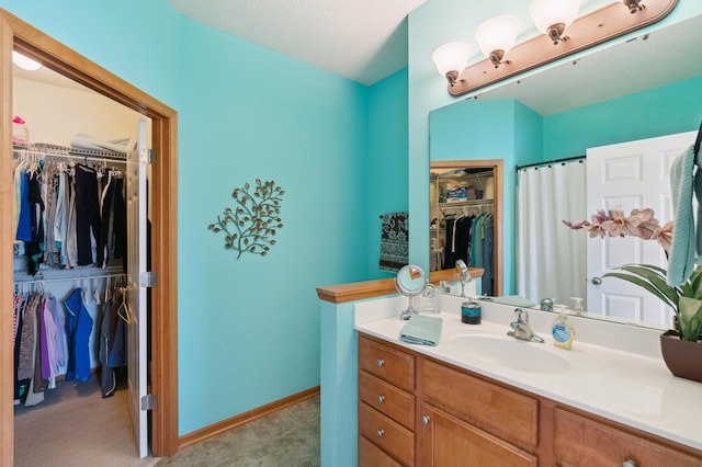 bathroom featuring a textured ceiling, vanity, baseboards, and a spacious closet