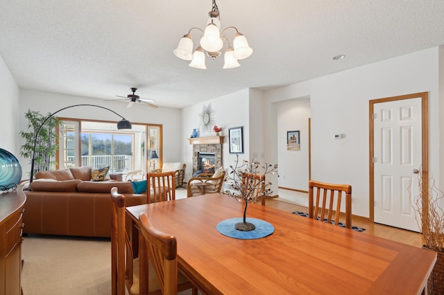 dining area with a textured ceiling, a stone fireplace, ceiling fan with notable chandelier, and baseboards