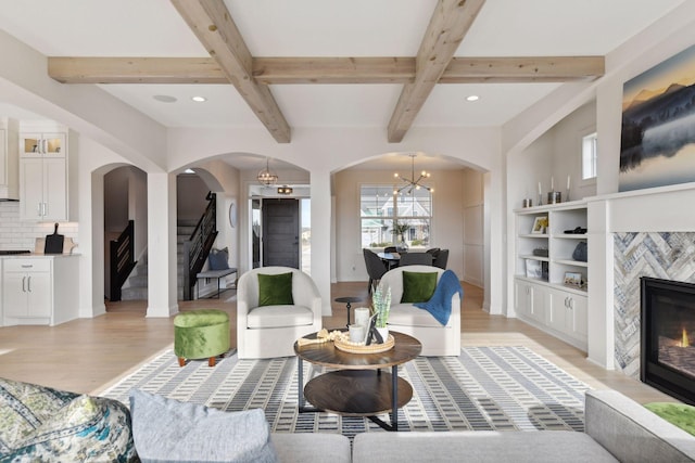 living room featuring light hardwood / wood-style flooring, beam ceiling, a high end fireplace, and a chandelier