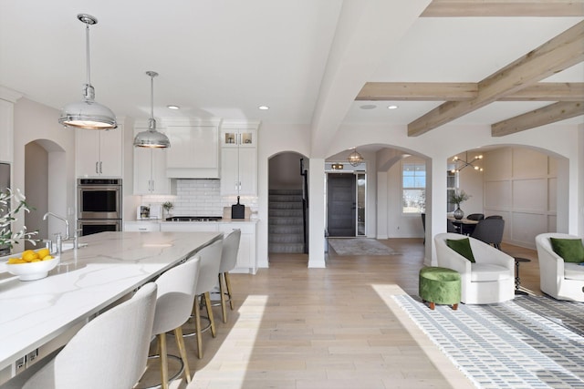 kitchen with hanging light fixtures, light stone counters, tasteful backsplash, white cabinets, and stainless steel double oven