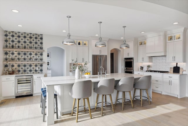 kitchen featuring appliances with stainless steel finishes, decorative light fixtures, white cabinetry, beverage cooler, and a large island with sink