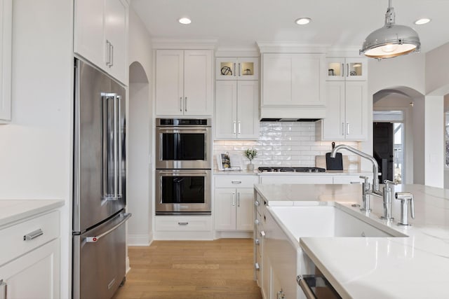 kitchen with white cabinetry, pendant lighting, stainless steel appliances, light hardwood / wood-style floors, and wall chimney range hood