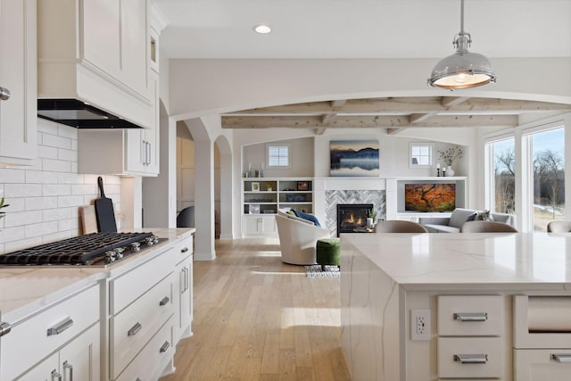 kitchen featuring pendant lighting, a tile fireplace, white cabinetry, light stone counters, and stainless steel gas cooktop