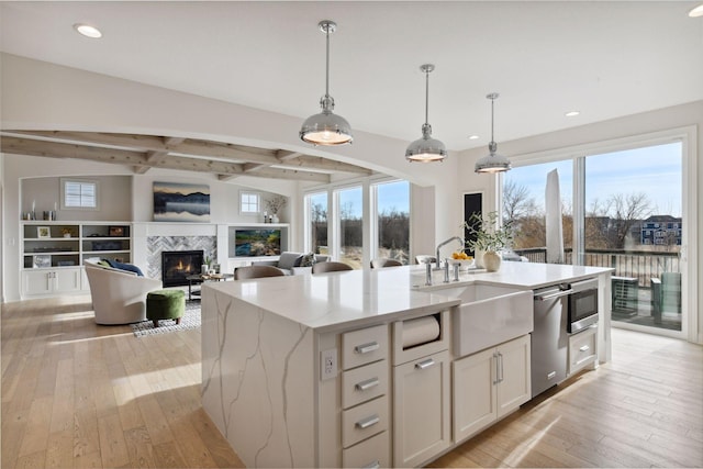 kitchen with pendant lighting, an island with sink, sink, white cabinets, and light stone countertops