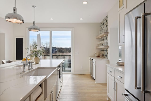 kitchen with high quality fridge, decorative light fixtures, white cabinetry, light stone countertops, and light wood-type flooring