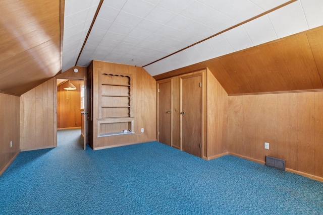 additional living space with lofted ceiling, dark carpet, wooden walls, and built in shelves