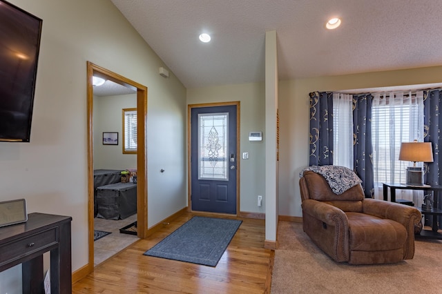 entryway with vaulted ceiling, a textured ceiling, and light hardwood / wood-style floors