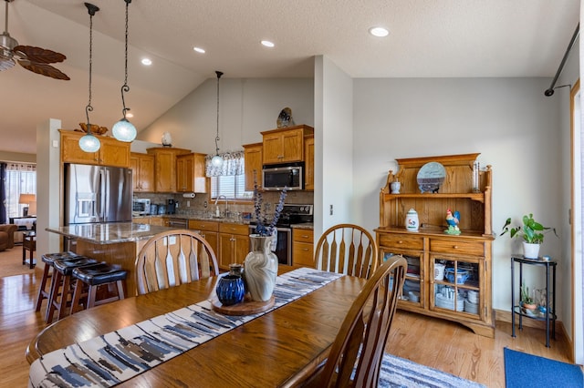 dining room featuring high vaulted ceiling, sink, ceiling fan, a textured ceiling, and light hardwood / wood-style flooring