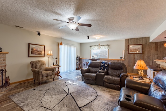 living room with ceiling fan, hardwood / wood-style floors, a textured ceiling, and wooden walls