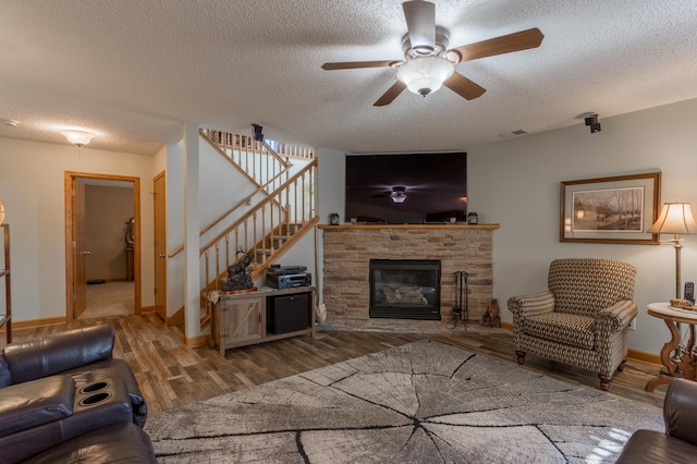 living room featuring hardwood / wood-style flooring, ceiling fan, a fireplace, and a textured ceiling