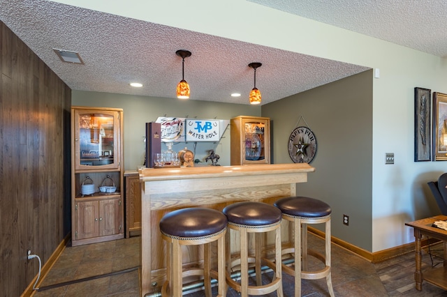 bar featuring pendant lighting, a textured ceiling, and wood walls